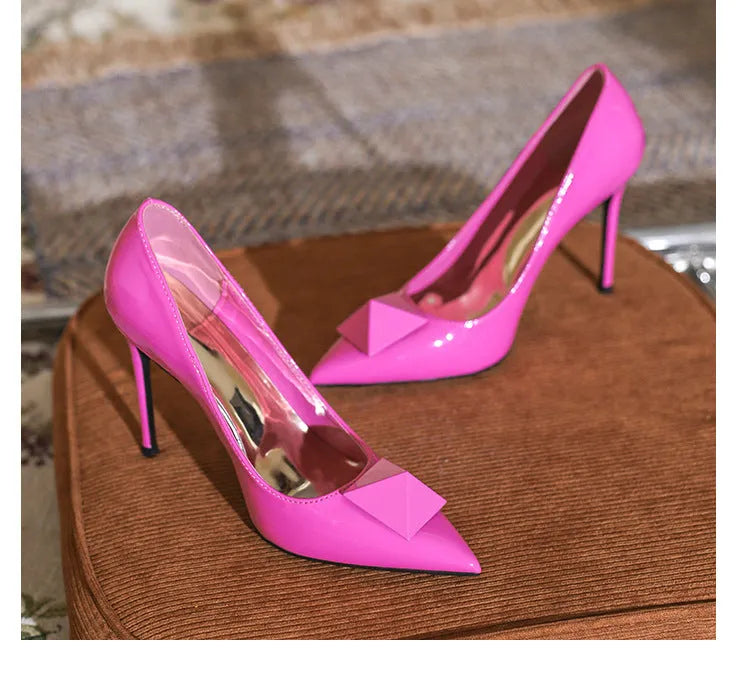 Pink patent leather women's pointed toe stiletto high heels with a rivet buckle.
