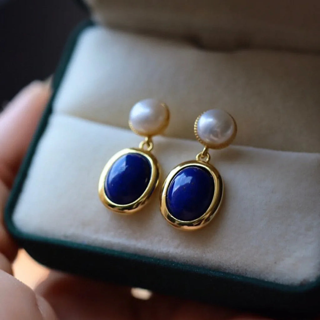 A pair of simple stud earrings with a blue lapis lazuli pearl set in a sterling silver setting.