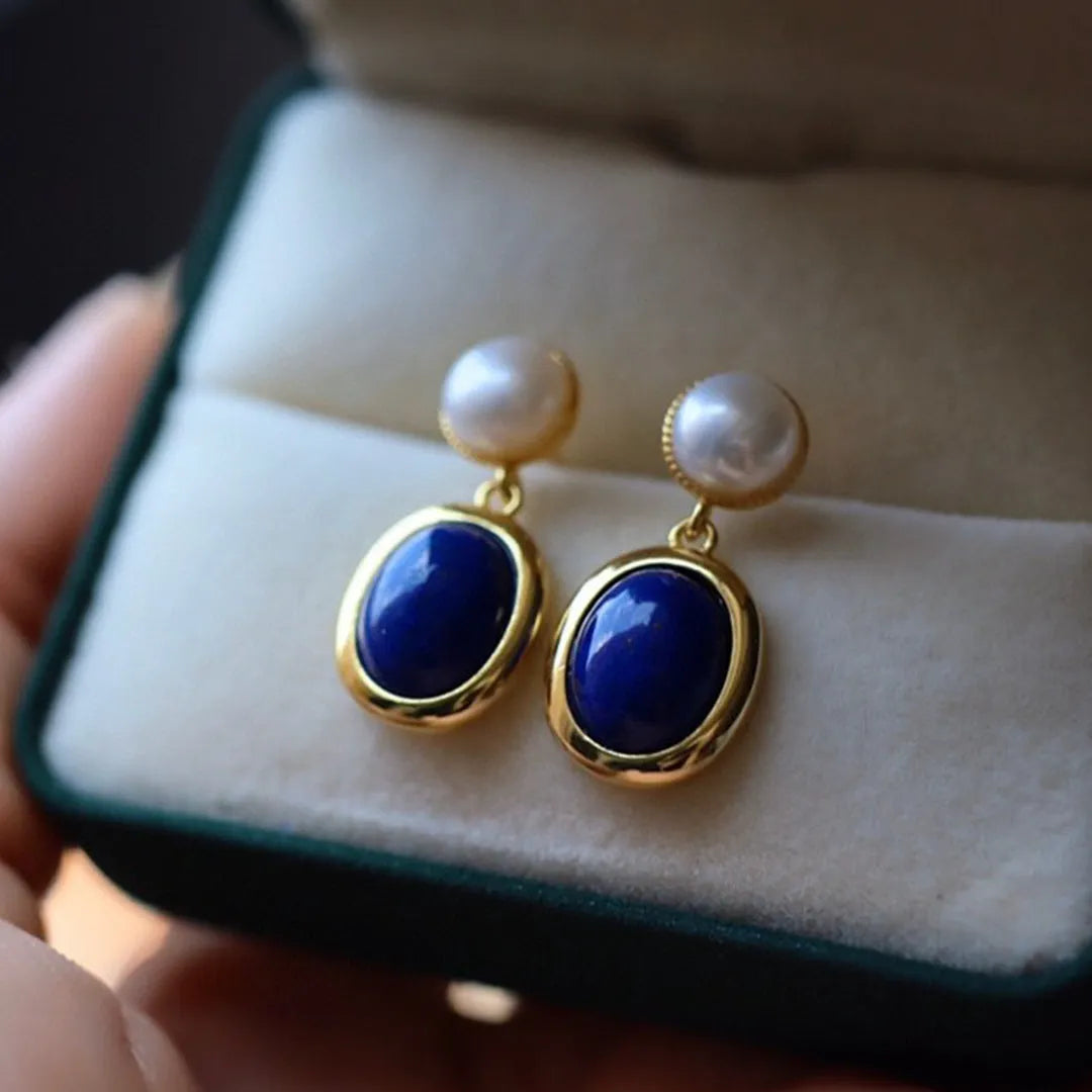 A pair of simple stud earrings with a blue lapis lazuli pearl set in a sterling silver setting.