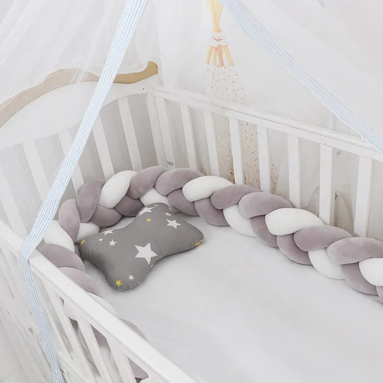 Braided knot style baby crib bumper in a light grey colour, shown lined inside a white wooden cot.