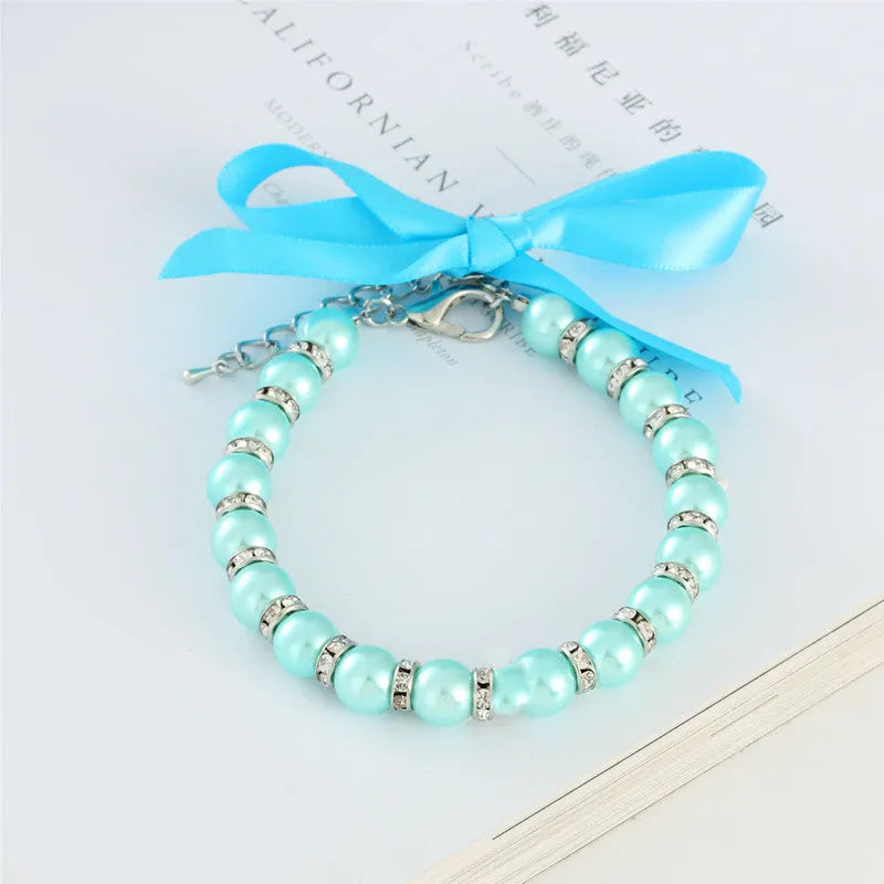 Small dog wearing blue imitation pearl and rhinestone necklace with adjustable clasp and ribbon bow