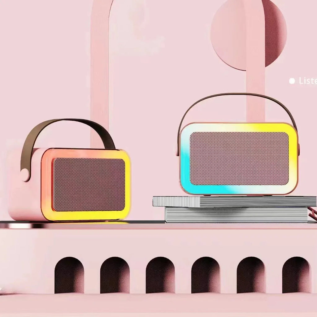 Pink portable Bluetooth karaoke speaker with microphone and coloured lights on a desk.