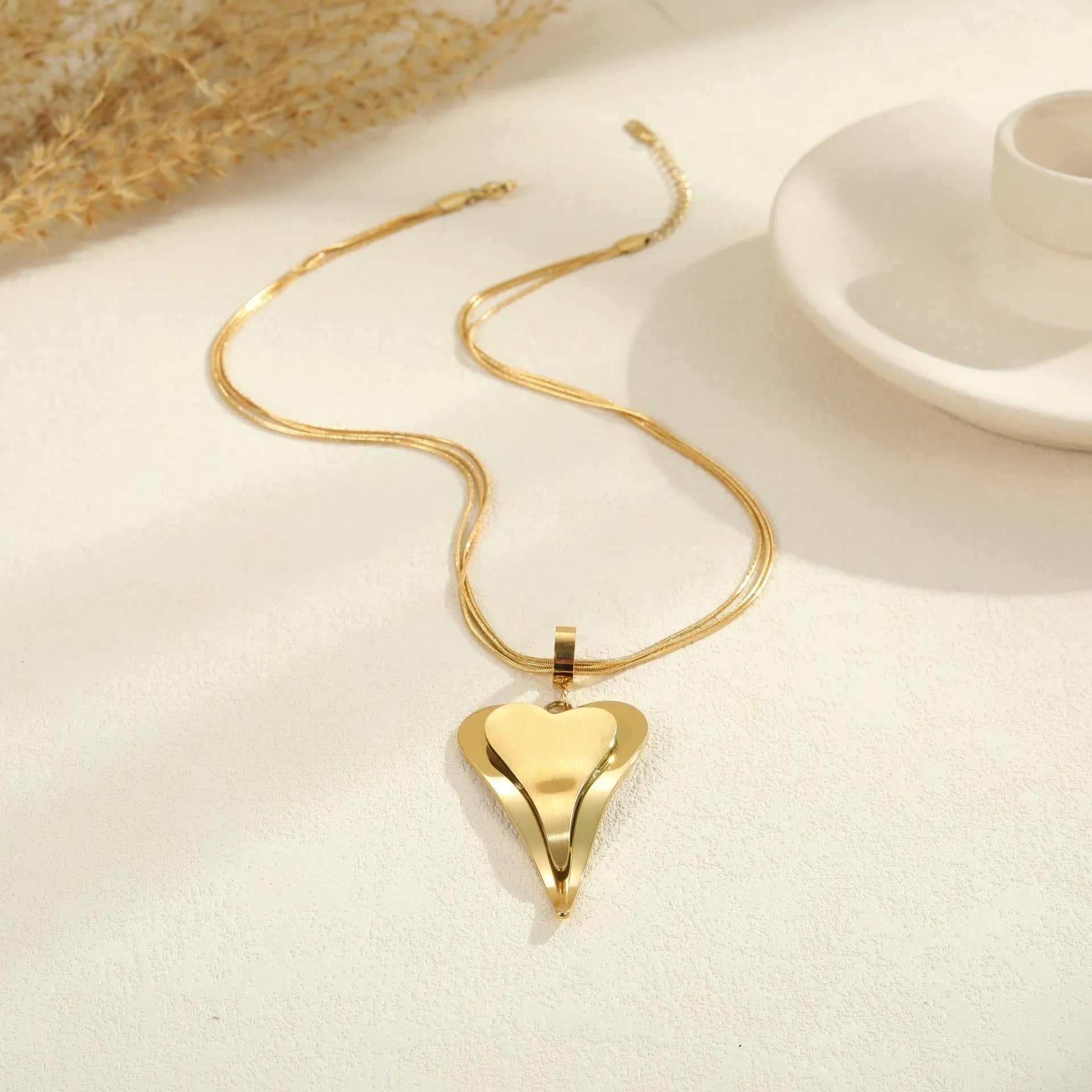 Close-up of a women's stainless steel necklace with a geometric double heart and snake bones chain design.