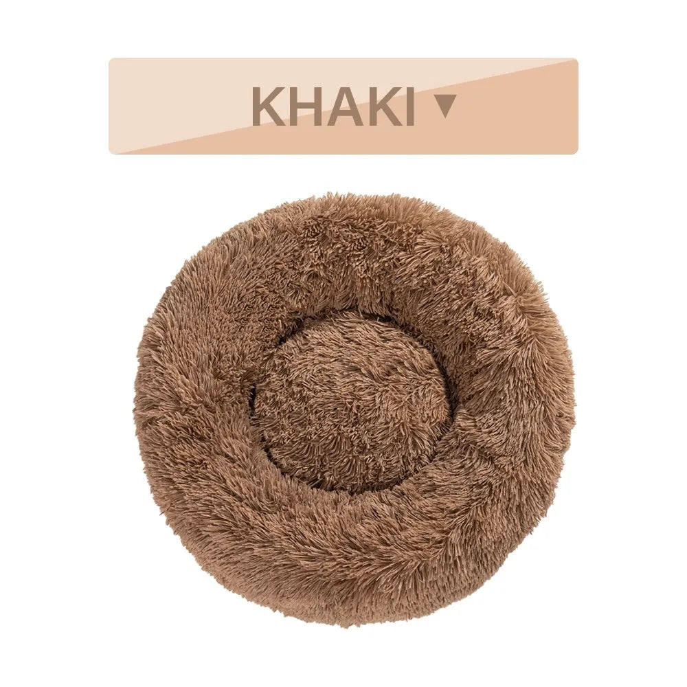 Fluffy donut-shaped dog bed in long plush fabric, shown in a light grey colour with a raised edge.