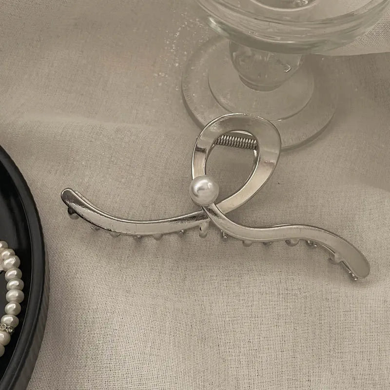 Assortment of silver metal hair claw barrettes with various designs including bows, pearls, and geometric shapes.