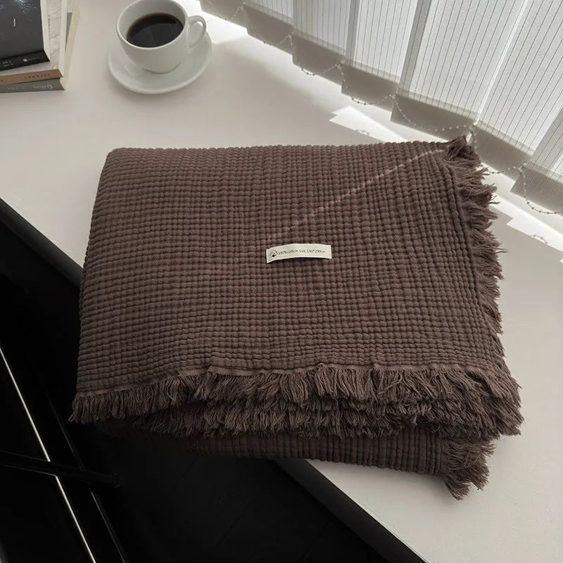 Four-layer gauze cotton blanket with tassel trim in avocado green colour draped over a sofa