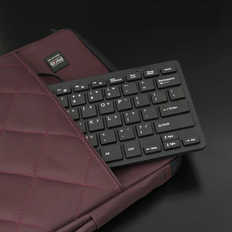 Compact black wired USB keyboard with noiseless keys next to notebook computer