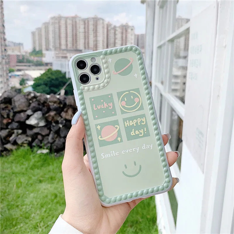Green TPU iPhone case with geometric smiley face and polka dot frame design on a table.
