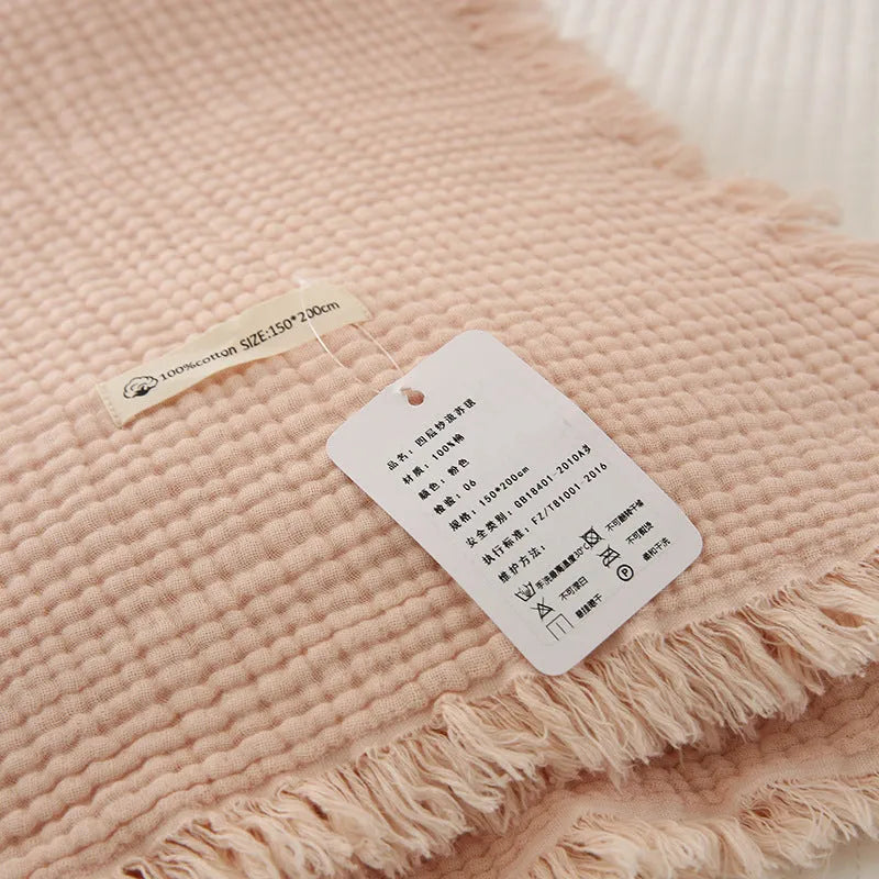 Four-layer gauze cotton blanket with tassel trim in avocado green colour draped over a sofa