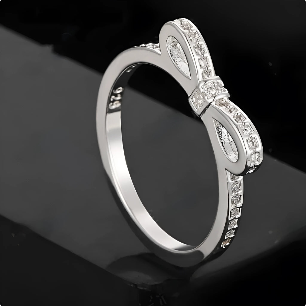 Silver electroplated bow-shaped ring with zircon crystal stones on a finger.