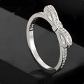 Silver electroplated bow-shaped ring with zircon crystal stones on a finger.