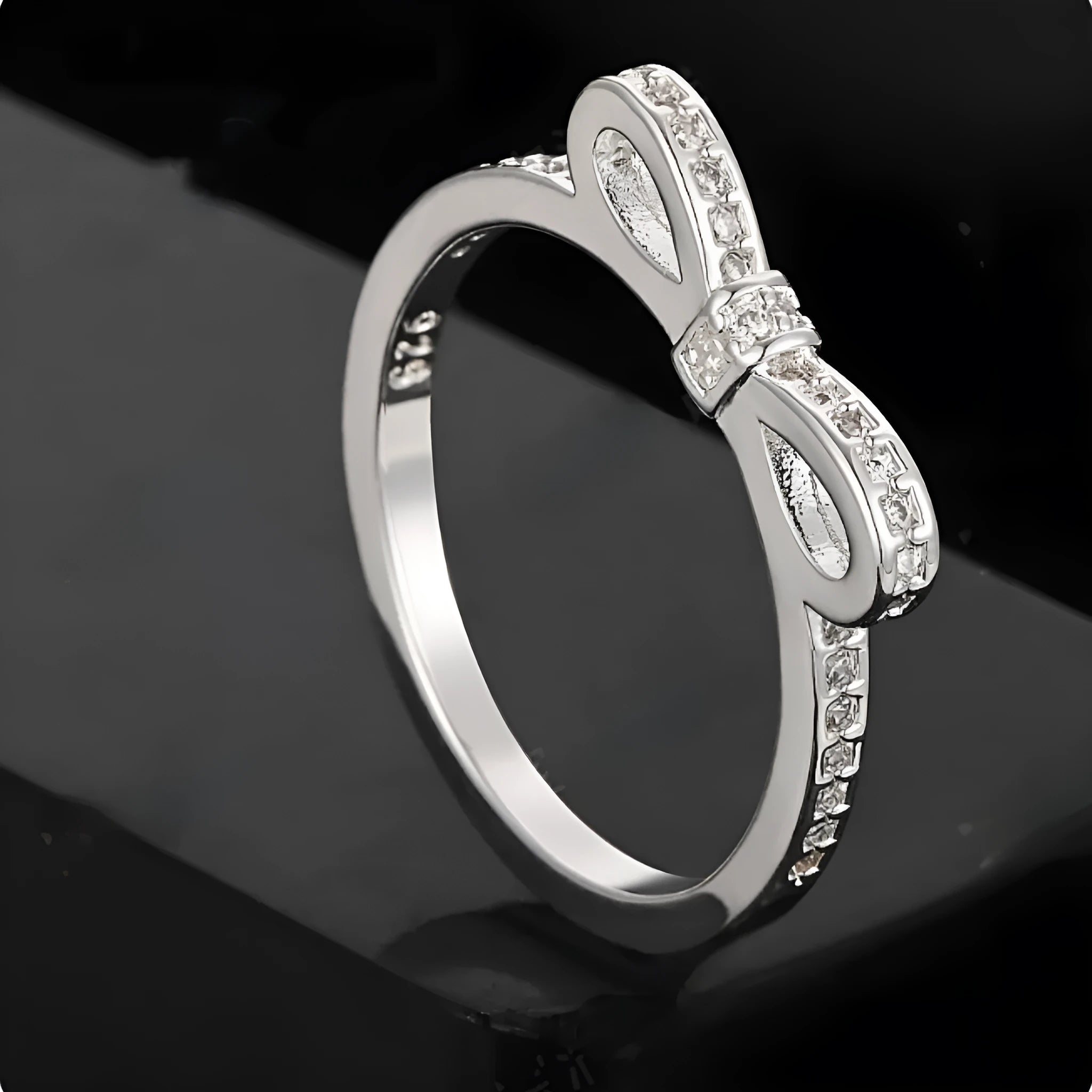 Silver electroplated bow-shaped ring with zircon crystal stones on a finger.