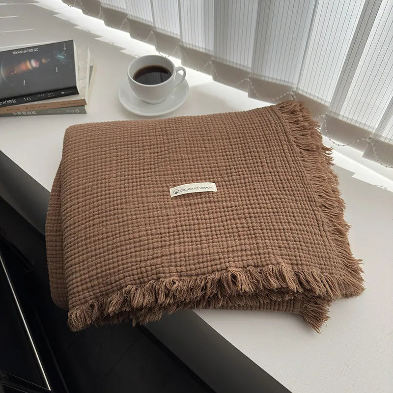 Four-layer gauze cotton blanket with tassel trim in avocado green colour draped over a sofa