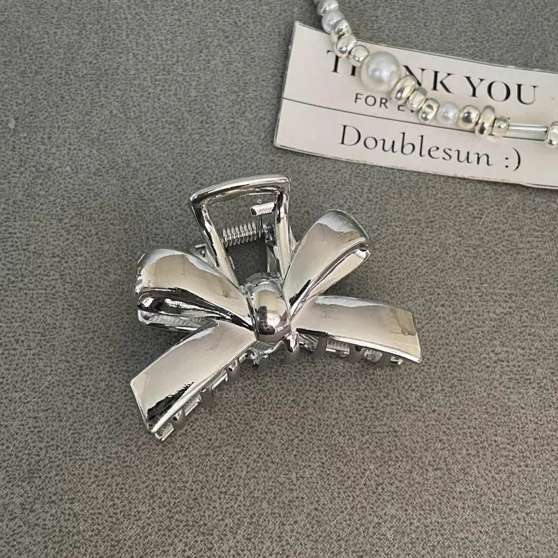 Assortment of silver metal hair claw barrettes with various designs including bows, pearls, and geometric shapes.