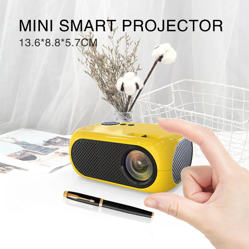 Compact gold or white M24 micro mini LED projector on a table with power adapter and AV cable.