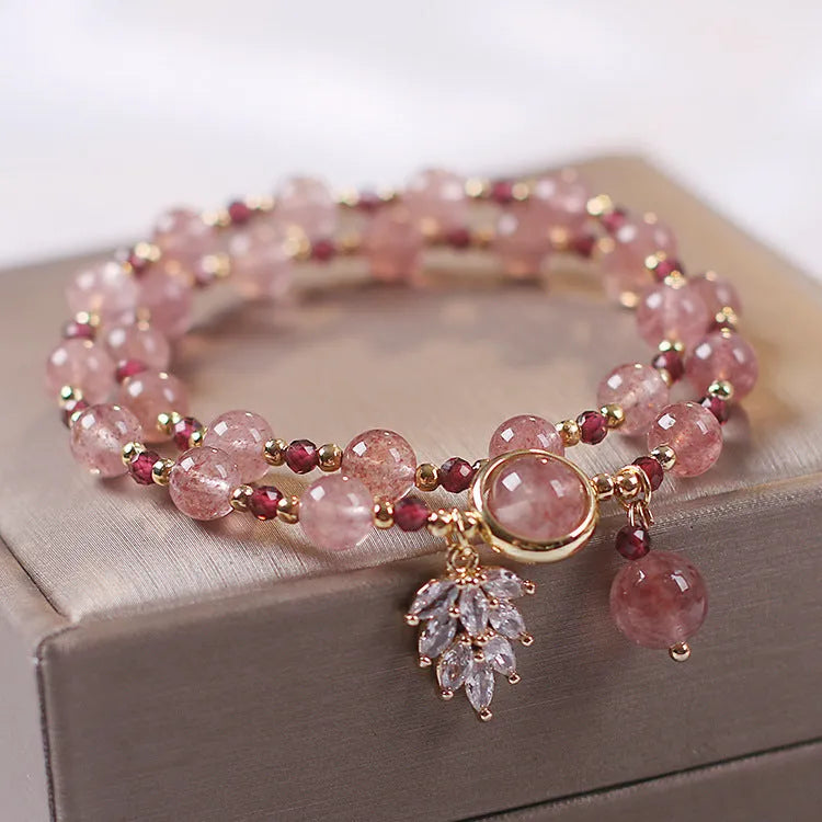Women's double-layer strawberry quartz crystal bracelet with a red lucky cat charm on a white background.