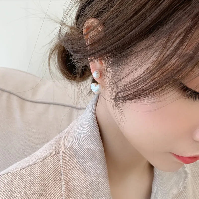 Close-up of simple heart-shaped alloy stud earrings with inlaid artificial gemstones.
