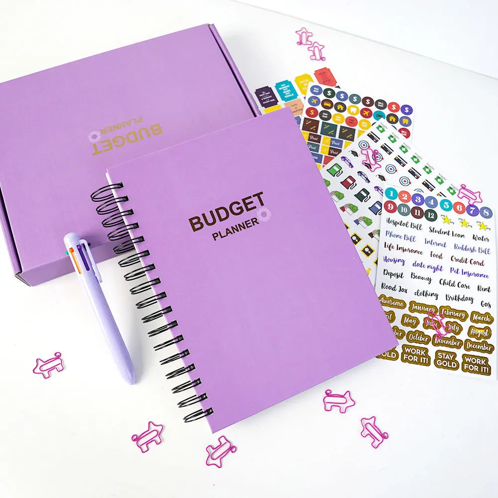 Purple coil-bound budget book open showing monthly financial planning layout with stickers and paper clips