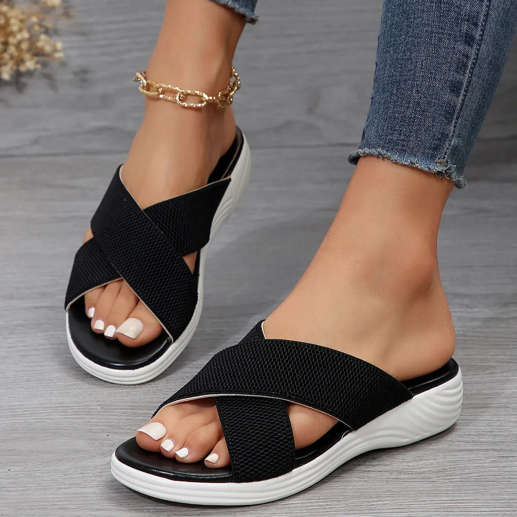 Women's black wedge slippers with a cross strap and peep toe on a thick rubber sole.