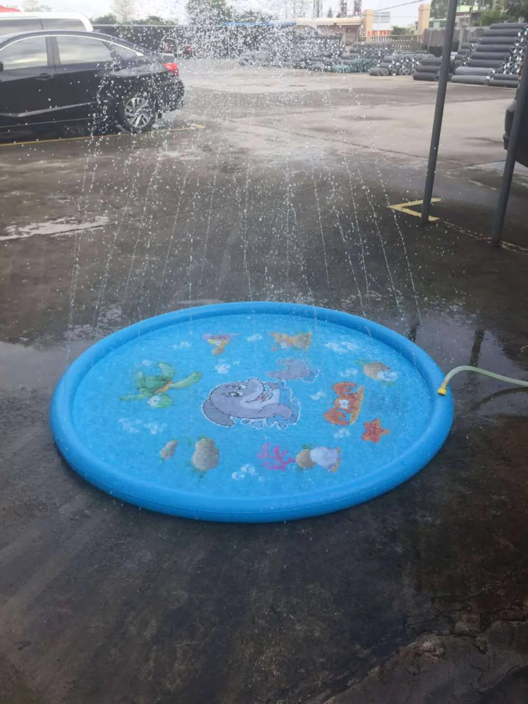 Blue PVC children's water spray mat with marine animal designs laid on grass, connected to a garden hose.