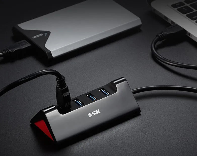 Black USB expansion dock with four ports on a desktop next to a laptop.