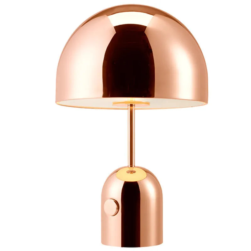 Mushroom-shaped table lamp with a metal base in rose gold finish on a wooden surface.
