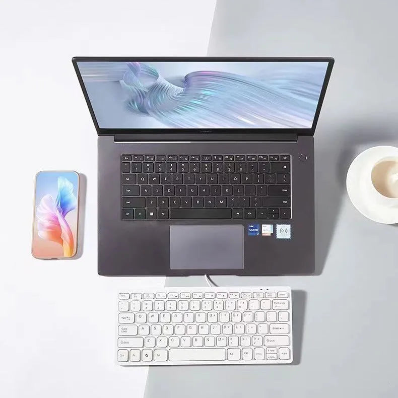 Compact black wired USB keyboard with noiseless keys next to notebook computer