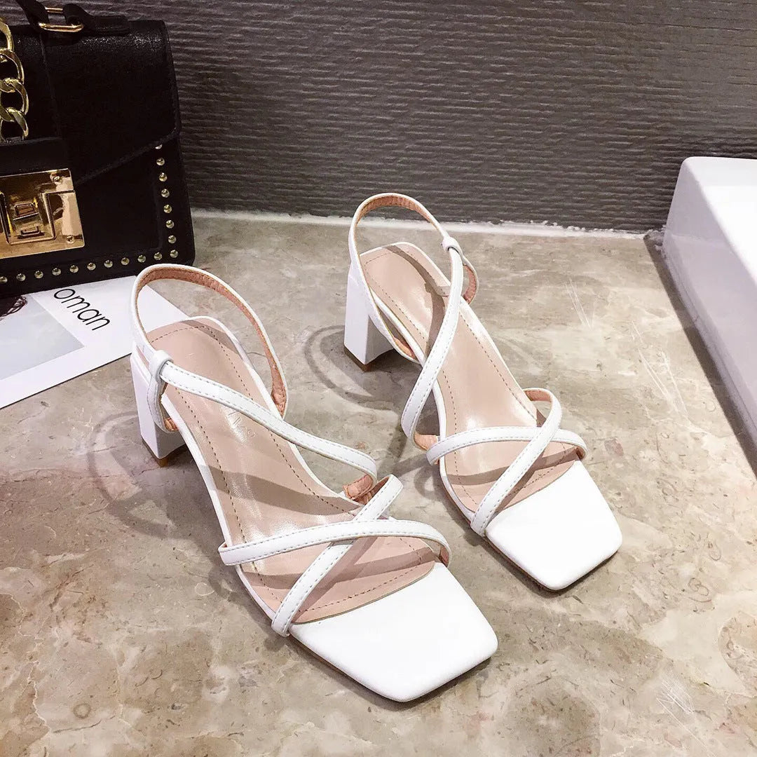 Women's white thick heel sandals with a backless design and side cut-outs on a wooden floor.