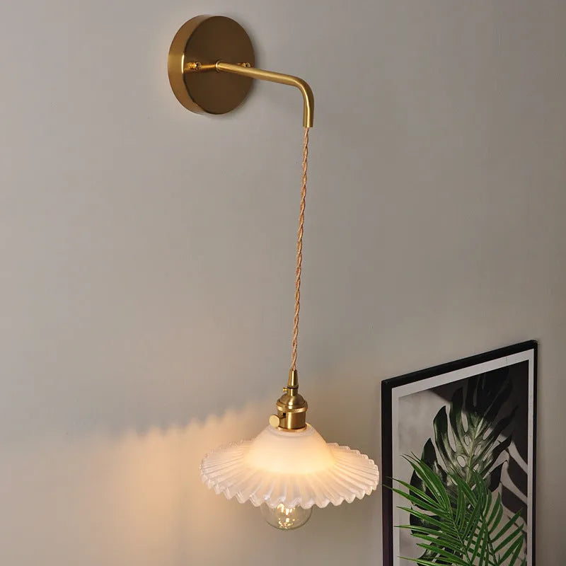 Brass lotus-shaped wall lamp with glass shade in choice of six colours on a plain wall.