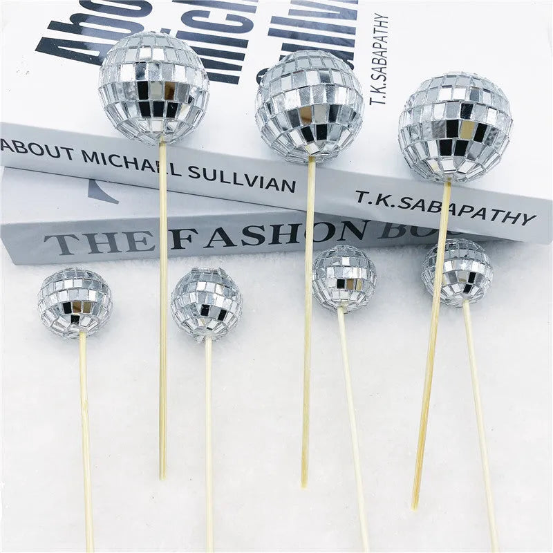 Glass mirror ball cake decoration on a wooden stick, showing reflective surface.