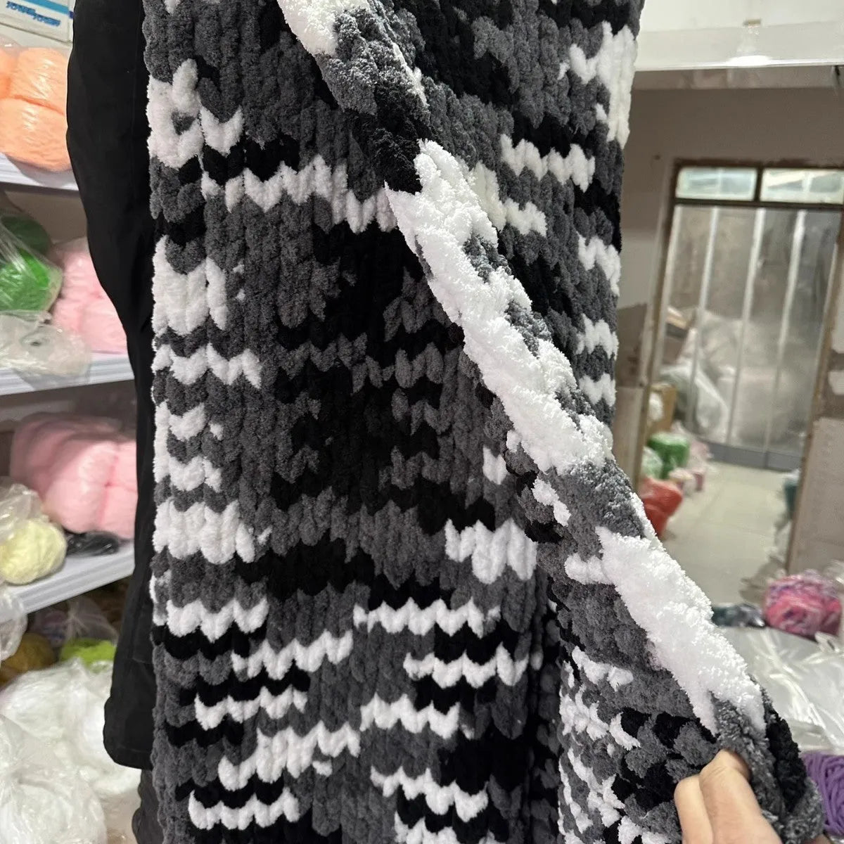 Coarse yarn chenille knitted blanket with braided gravity trim in a modern colour on a bed.