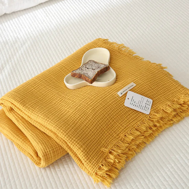 Four-layer gauze cotton blanket with tassel trim in avocado green colour draped over a sofa