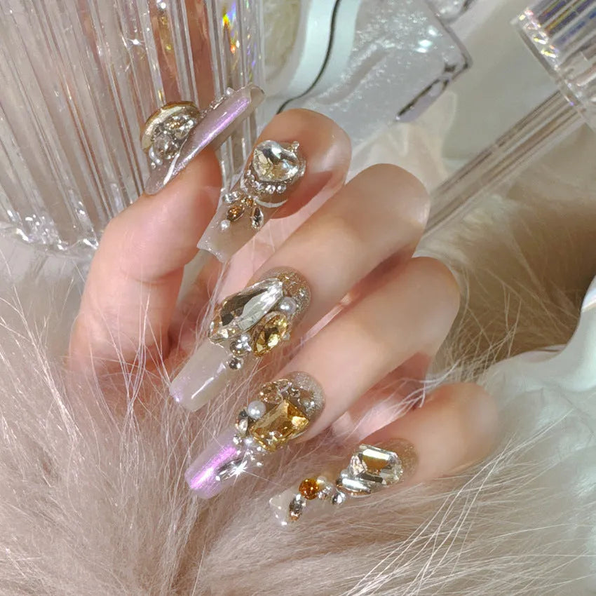 False nail patches with large rhinestones on card, shown with jelly adhesive pot and nail tools.
