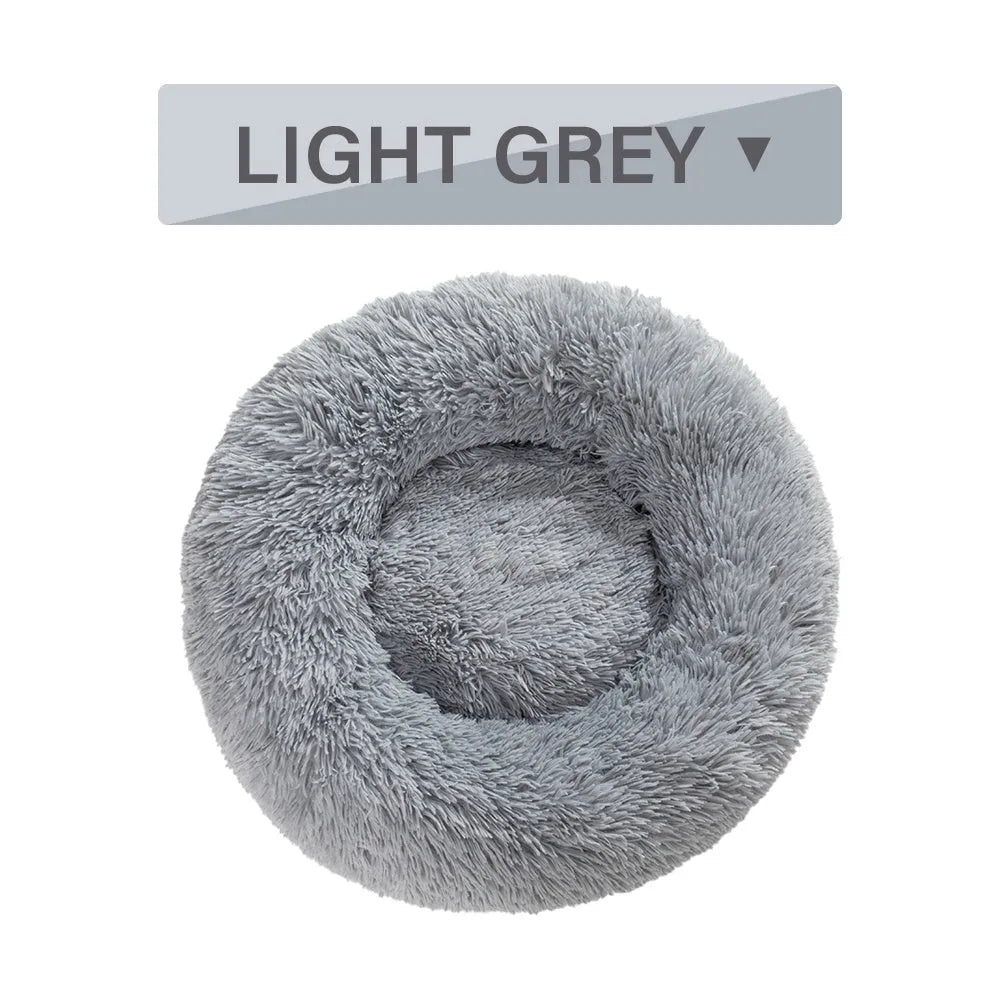 Fluffy donut-shaped dog bed in long plush fabric, shown in a light grey colour with a raised edge.