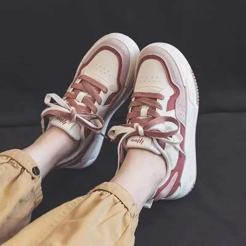 Women's pink and white low top imitation leather sneaker with rubber sole on a neutral background.