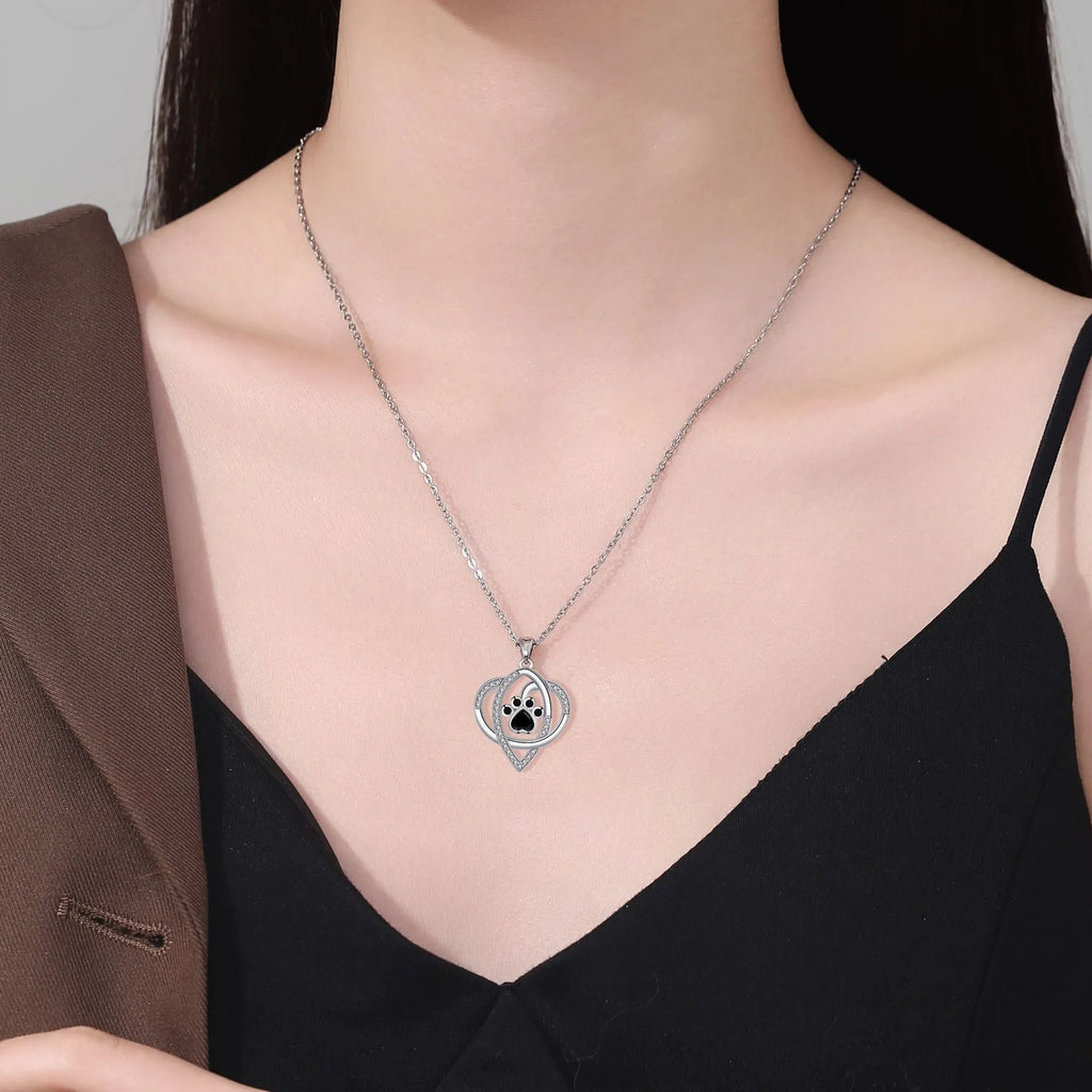 Close-up of a copper necklace pendant showing detailed cat and dog paw prints on a cross chain.