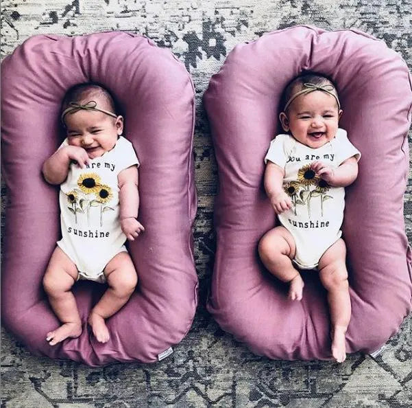 Beige portable baby nest crib cot for newborn infant on a bed