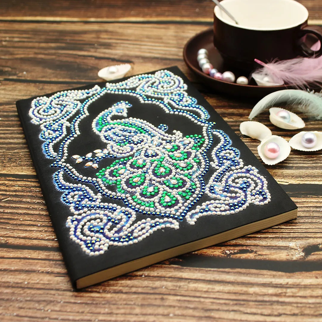 Black A5 notebook with a peacock design made from shaped and bright diamond painting drills.
