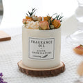 Aromatherapy candle decorated with dried flowers on top, shown in gift box packaging with a wood base.