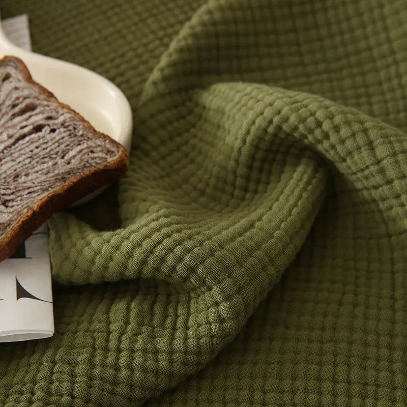 Four-layer gauze cotton blanket with tassel trim in avocado green colour draped over a sofa