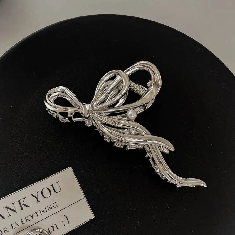 Assortment of silver metal hair claw barrettes with various designs including bows, pearls, and geometric shapes.