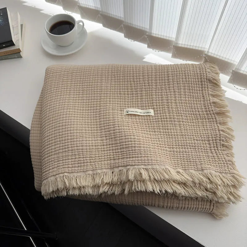 Four-layer gauze cotton blanket with tassel trim in avocado green colour draped over a sofa