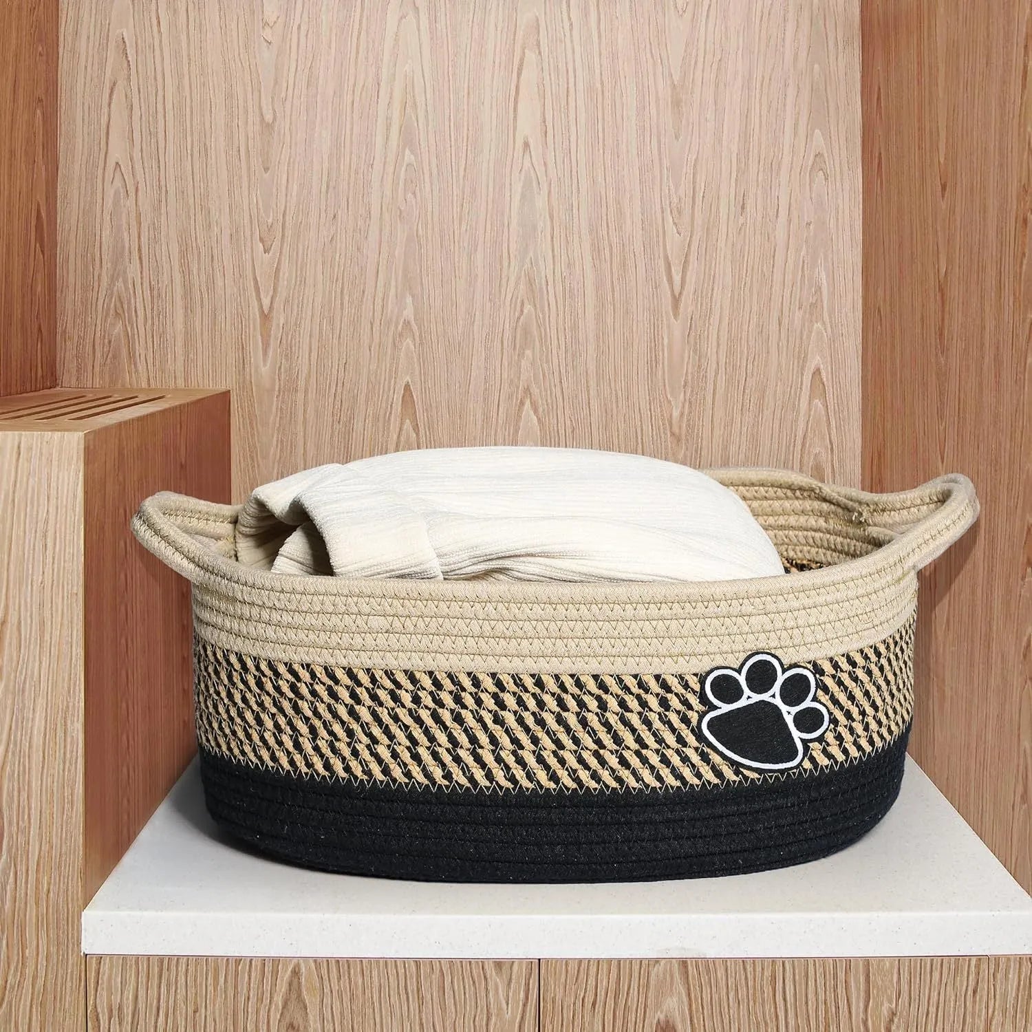 Light beige handmade cotton rope storage basket with wooden handle on a table.