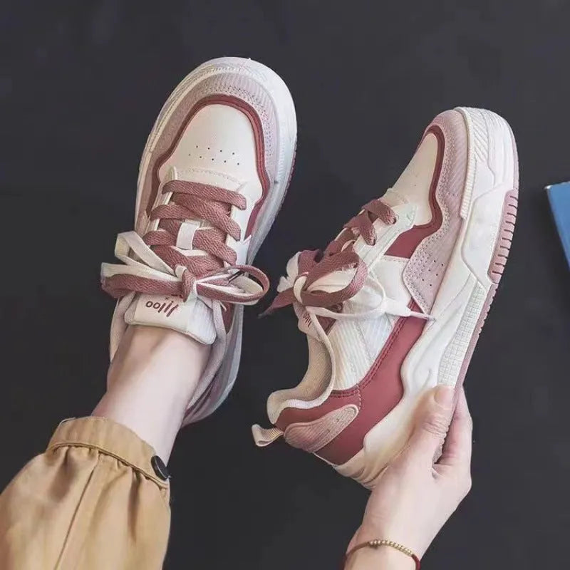 Women's pink and white low top imitation leather sneaker with rubber sole on a neutral background.