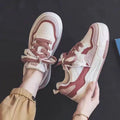 Women's pink and white low top imitation leather sneaker with rubber sole on a neutral background.