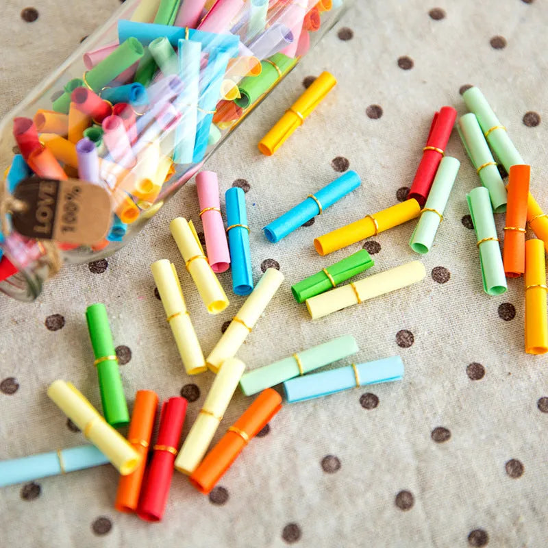 Colourful assortment of miniature rolled paper scrolls with metal eyelets for drift bottle messages.