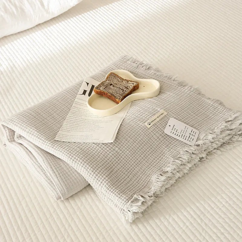 Four-layer gauze cotton blanket with tassel trim in avocado green colour draped over a sofa