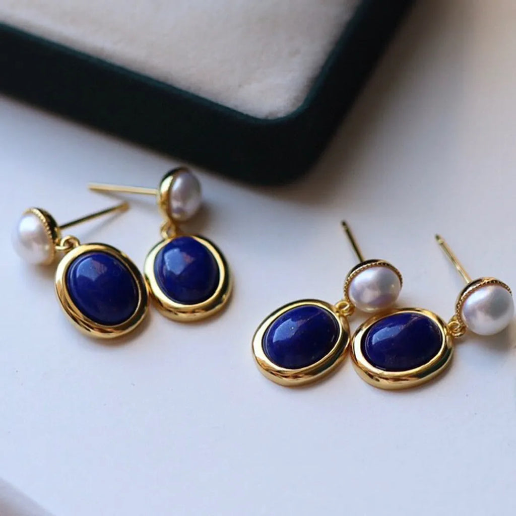 A pair of simple stud earrings with a blue lapis lazuli pearl set in a sterling silver setting.