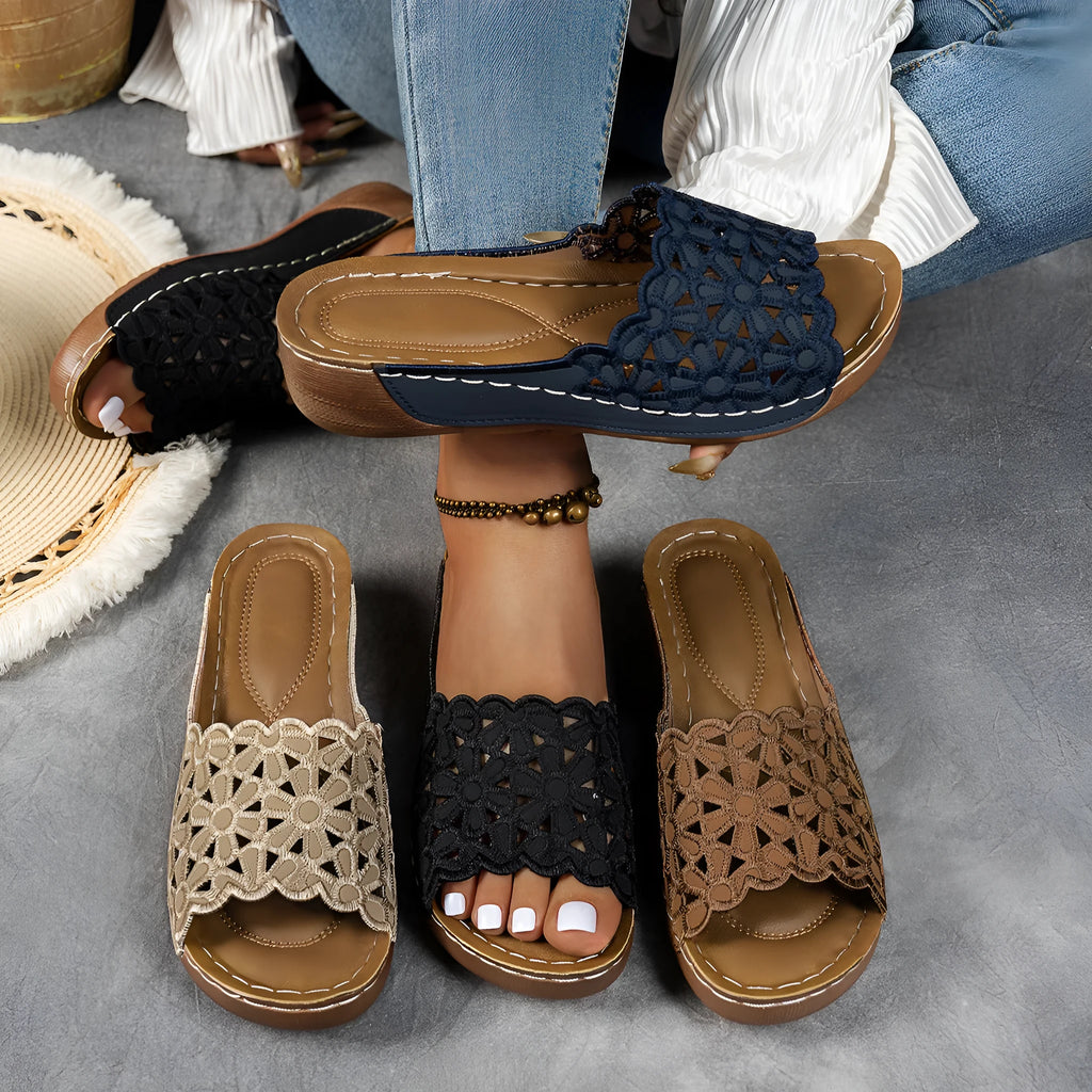 Women's black beach slipper with flower cutouts, a fish mouth toe, and a low wedge heel on a rubber sole.