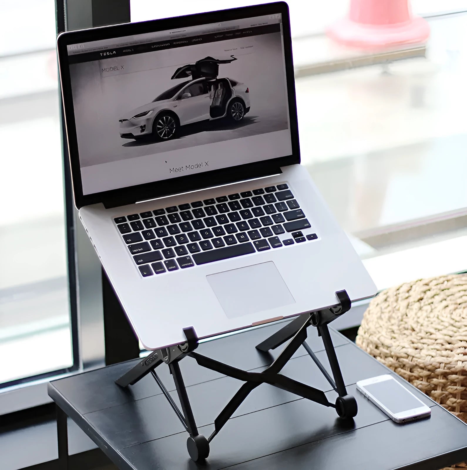 Black folding portable laptop stand made of reinforced nylon, shown both open for use and folded flat.